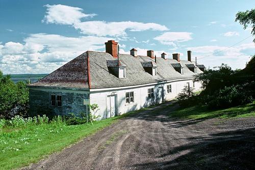 General view of Building 16 showing the wood frame hipped roof with dormers and masonry chimneys, circa 2004.; Parks Canada Agency | Agence Parcs Canada, circa | vers 2004