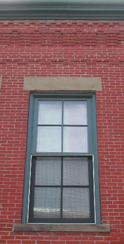 This photograph shows an upper storey window sandstone lintel and sill, as well as the corbel band at the roof-line cornice, 2005; City of Saint John