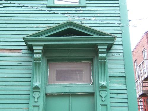 This photograph shows the entablature with pointed pediment over the entrance, the long ornate brackets and the transom window, 2005; City of Saint John