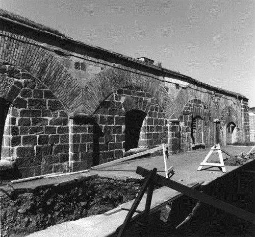 View of the façade of Building 21, showing the six large, low arches supported by pilasters, each opening is topped by a stone arch, circa 1980.; Department of National Defence / Ministère de la Défense nationale, circa 1980.