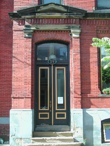 This photograph shows the entrance to the building, and illustrates the pedimented entablature, transom window, and detailed brick work, 2005; City of Saint John