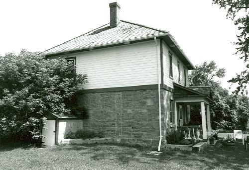 Corner view of the Defensible Lockmaster's House, showing the exterior walls of the ground floor constructed of limestone masonry and those of the frame second floor clad in clapboard, 1989.; Parks Canada Agency / Agence Parcs Canada, Couture, 1989.