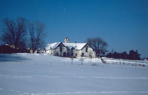 View of the front façade of the Stable, showing the placement of the doors and large round-topped windows, 1991.; Parks Canada Agency / Agence Parcs Canada, E. Tumark, 1991.