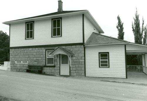 Side view of the Lower Brewers Defensible Lockmaster's House, showing the thick ground floor wall constructed of evenly coursed limestone masonry with infilled loopholes, and the frame second floor clad in clapboard, 1989.; Department of Public Works / Ministère des Travaux publics, 1989.