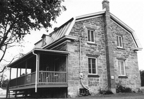 General view of the Collector's House, showing its low, two-storey massing with fairly wide gable walls and a gambrel roof with dormers, 1989.; Parks Canada Agency / Agence Parcs Canada, 1989.