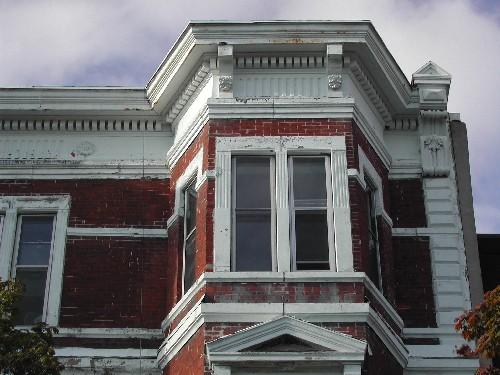 This photograph shows the large cornice, brackets, dentils, and wide frieze band. It also illustrates the quoins and a pedimented entablature over the second storey window, 2005; City of Saint John
