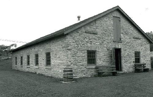 Corner view of the Foundry, showing the exterior walls of rubblework, the placement of the simply detailed door and windows, with voussoirs and dressed stone sills, 1989.; Public Works and Government Services Canada / Travaux publics et Services gouvernementaux Canada, 1989.