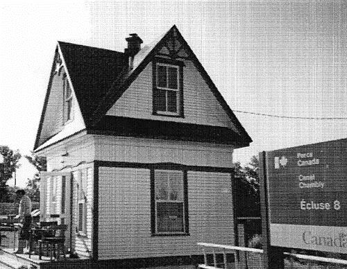 General view of Lockstation Cabin 8, showing the steep roof, the contrasting textures and colours adorning the wood siding, and the small pediments over the doors and windows, 1993.; Parks Canada Agency / Agence Parcs Canada, 1993.