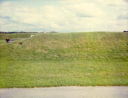 View of the side of RMC Building 30b, showing the entrance to the left and the unaltered combination of unobtrusive earthwork and minimal architectural visibility in accordance with its original purpose to store dangerous explosives, 1993.; Parks Canada Agency / Agence Parcs Canada, 1993.