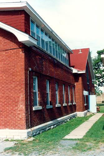 View of the side façade of RMC Building 36, showing the stone base typical to the buildings of the immediate complex and other structures nearby, 1993.; Parks Canada Agency / Agence Parcs Canada, 1993.