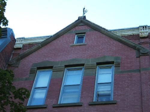 This photograph shows one of the flush gables that extend above the roof-line cornice, and illustrates the sandstone tracery that connects the lintels of the windows, 2005; City of Saint John