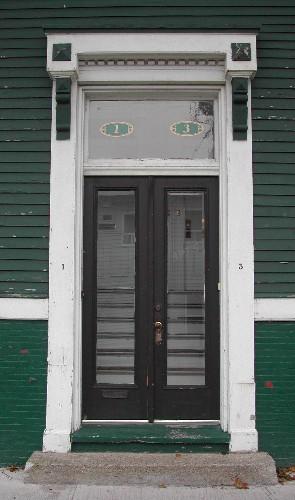 This image provides a view of one of the Orange Street entries including an entablature with brackets, dentils and pilasters, a transom window and paired wood doors with glass panels, 2005; City of Saint John