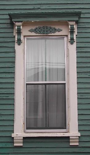 This image provides a view of a vertical sliding wood window below an entablature supported by ornate brackets, 2005; City of Saint John