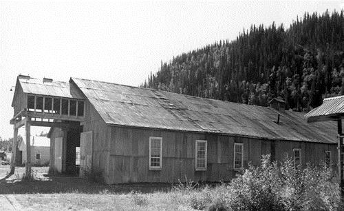 General view of the Machine Shop, showing its simple rectangular shape, its gable roof and its corrugated metal siding and roof covering, 1988.; Parks Canada Agency / Agence Parcs Canada, 1988.