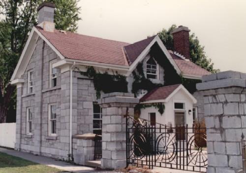 General view of RMC Building 6, showing the house-form, stone clad, gable-roofed block with a central gable on the front and the rear and the end chimneys, 1993.; Parks Canada Agency / Agence Parcs Canada, 1993.