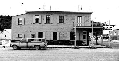 Side view of the Bank of British North America, showing details such as the ornate, Victorian-style front doors set into the salient angle, and the overhanging corner balcony supported on slender, turned porch columns, 1988.; Parks Canada Agency / Agence Parcs Canada, J. Mattie, 1988.