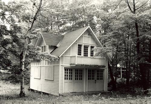 View of the exterior of the Garage and Servant's Quarters, showing the small balcony above the garage doors on the second level, 1984.; Parks Canada Agency / Agence Parcs Canada, M. Trépanier, 1984.