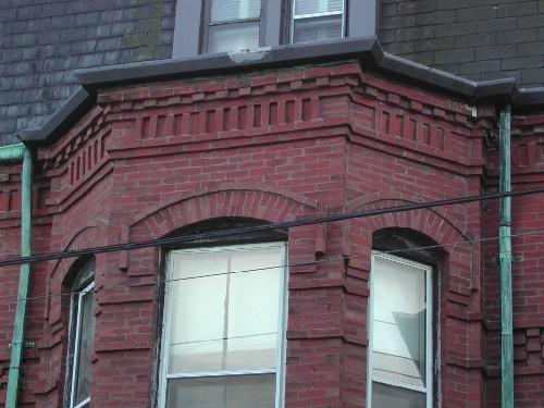 This photograph shows the cornice over one of the bay windows, the dentils, the segmented arch openings and the brickwork of the fascia, 2005 ; City of Saint John