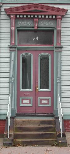 This image provides a view of the entrance with a pedimented entablature, brackets, pilasters, a transom window and paired wood doors with segmented arched glass panels, 2005; City of Saint John