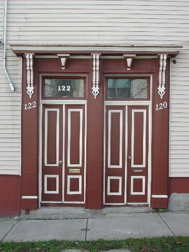 This photograph shows the double entrances of the building, the transom windows, and the ornate bracketed entablature, 2005; City of Saint John