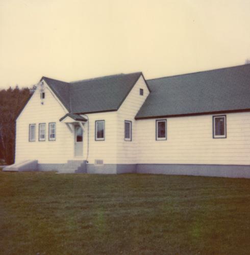 View of the exterior of the Administration Building, showing its wood components including the shingles of the wall and the wooden multi-pane sash windows, 1990.; Parks Canada Agency / Agence Parcs Canada, 1990.