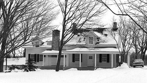 General view of the Farm House, showing the three-bay wide structure with a large wing addition, front verandah and gable roof with dormers and stone chimneys.; Parks Canada Agency / Agence Parcs Canada.