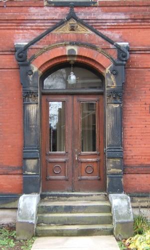 This image provides a view of the entrance consisting of a pediment, fluted pilasters with Corinthian capitals, a segemented arch transom window and paired wood doors with glass panels, 2005; City of Saint John