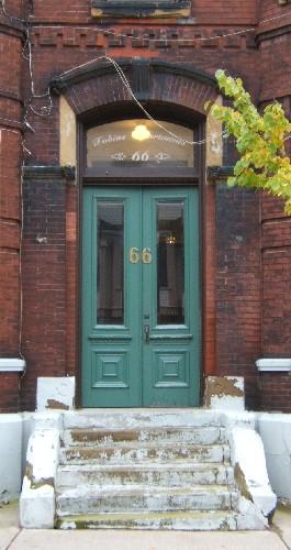 This image provides a view of the entrance consisting of a segmented arch brick and sandstone hood mold, a pronounced keystone, a segmented arched transom window and paired wood doors with glass panels, 2005
; City of Saint John