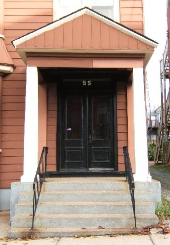 This image provides a view of the pedimented portico supported by pillars above a transom window and paired wood doors with glass panels, 2005
; City of Saint John