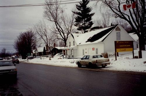 View of the exterior of the St. Laurent Store and Warehouse, showing the wood clapboard siding painted white and the gable roofs without dormers, 1993.; Parks Canada Agency / Agence Parcs Canada, 1993.