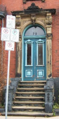This image provides a view of the entry consisting of an elaborate sandstone entablature supported by brackets, fluted pilasters with Corinthian capitals, a Roman arch transom window and paired wooden doors with glass panels, 2005; City of Saint John