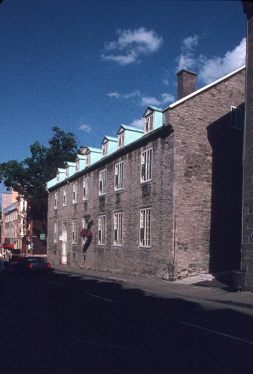 Corner view of the St. Louis Street front showing the consistent detailing including multi-pane casement windows, overlit doors set at street level, and contrasting stone quoins and sill.; Parks Canada Agency / Agence Parcs Canada