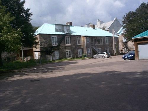 View of side façade of 63 St. Louis Street demonstrating the use of similar building materials including stone walls, tin roofing, and wood trim.; Parks Canada Agency / Agence Parcs Canada