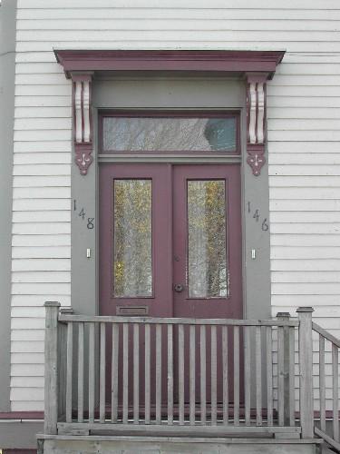 This photograph shows the entrance to the building, and illustrates the bracketed cornice and transom window over the paired wooden door with glass panels, 2005; City of Saint John