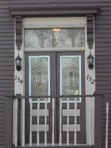 This photograph shows the entrance to the building, and illustrates the bracketed entablature over transom window and paired wooden doors with upper glass panels, 2005; City of Saint John