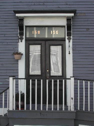 This photograph shows the entrance to the building, and illustrates the bracketed entablature over the transom window and the paired wooden doors with glass panels, 2005; City of Saint John