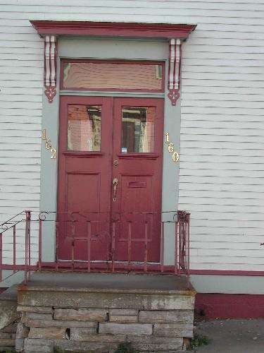 This photograph shows the entrance to the building, illustrating the bracketed entablature over the transom window and the double wooden doors with glass upper panels, 2005; City of Saint John