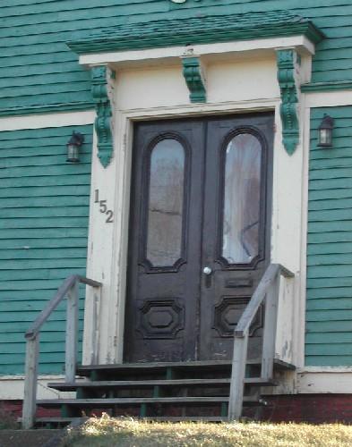 This image provides a view of the entry consisting of a wooden entablature supported by brackets above paired doors with Roman arched glass panels, 2006; City of Saint John