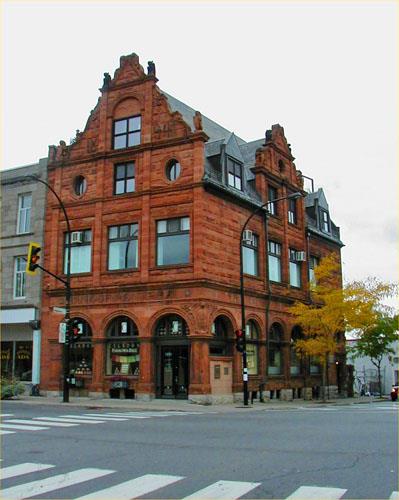 Corner view of the Bank of Montréal showing its fenestration such as a glazed arcade on the ground floor; large windows on the second floor; and a medley of oval, sash and dormer windows in the two attic storeys, 2004.; Parks Canada Agency / Agence Parcs Canada, 2004.