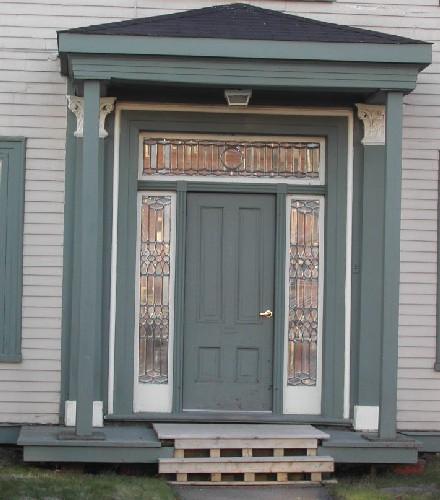 This image provides a view of the central entry with a hipped roof, Corinthian pilasters, stained glass transom window, sidelights and wooden paneled door, 2006; City of Saint John