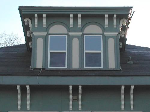 This image provides a view of the central dormer with a hipped roof encasing two Roman arched openings above wide eaves supported by a series of paired, scrolled brackets, 2006
; City of Saint John