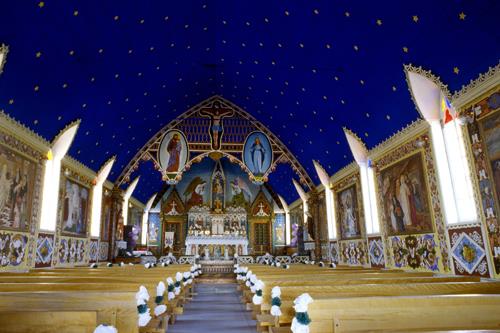 View of the interior of the Church of Our Lady of Good Hope emphasizing the Gothic style painted decoration of interior, including ornamentation surrounding figural panels and ornamented wainscotting, painted floor, painted tripartite arch motif at altar.; Parks Canada Agency / Agence Parcs Canada, n.d.