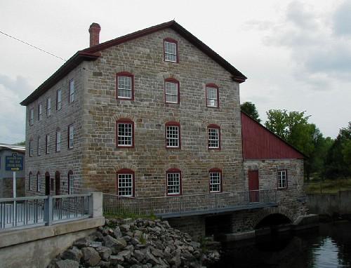 Side view of the Old Stone Mill, showing its masonry construction with exterior walls of uneven coursed local stone with heavy stone corner quoins, 2004.; Parks Canada Agency / Agence Parcs Canada, 2004.