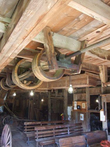 Interior view of first floor, including pulleys used to drive various machines, Sutherland Steam Mill Museum, Denmark, NS, August, 2008. Also included are several school desks produced jointly by the mill and the Brule Foundry.; Dept. of Tourism, Culture and Heritage, Province of Nova Scotia, 2008