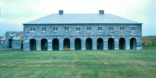 General view of Fort Lennox showing the buildings, their stone construction, their volume, mass, roof type, window and door placements.; Parks Canada Agency / Agence Parcs Canada.