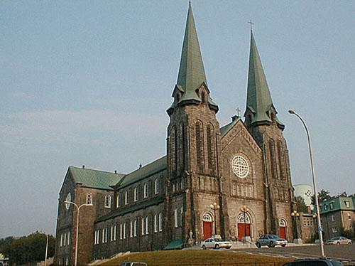 Facade and corner view of the Cathedral.  It illustrates the two spires, the central nave with its stained glass as well as the lateral nave.; PNB 2003