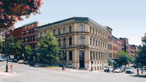 View of the the primary entrance of the building on the corner of two streets. The storeys and windows lessen in height from the preceding storeys giving the illusion of a taller building; Commercial Properties Limited