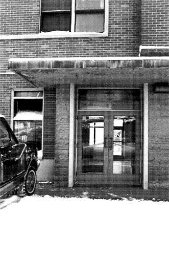 Detail view of the Canadian National Railways Station's main public entrance, offset beside the stair tower, showing the three panel wooden and glass doors, 1996.; Parks Canada Agency / Agence Parcs Canada, S. D. Bronson, 1996.