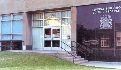 Detail view of the main entrance to the Government of Canada Building showing the lack of ornamentation, use of simple construction materials and smooth surfaces.; Parks Canada Agency / Agence Parcs Canada, n.d.