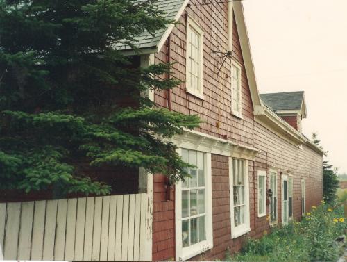 Showing wood shingled exterior and bracketed cornice above ground floor windows; Province of PEI